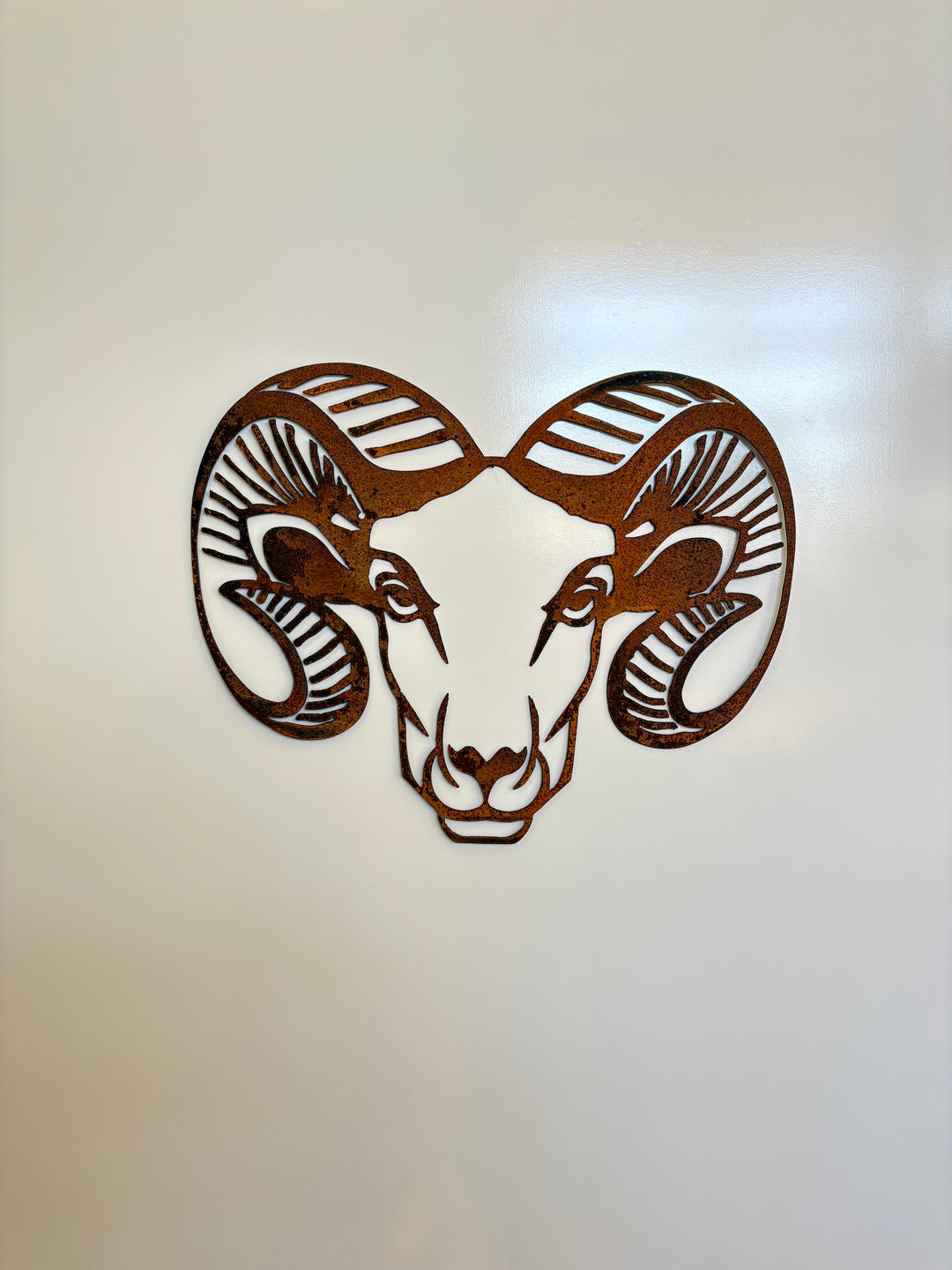 Metal wall art of a ram's head on a plain background